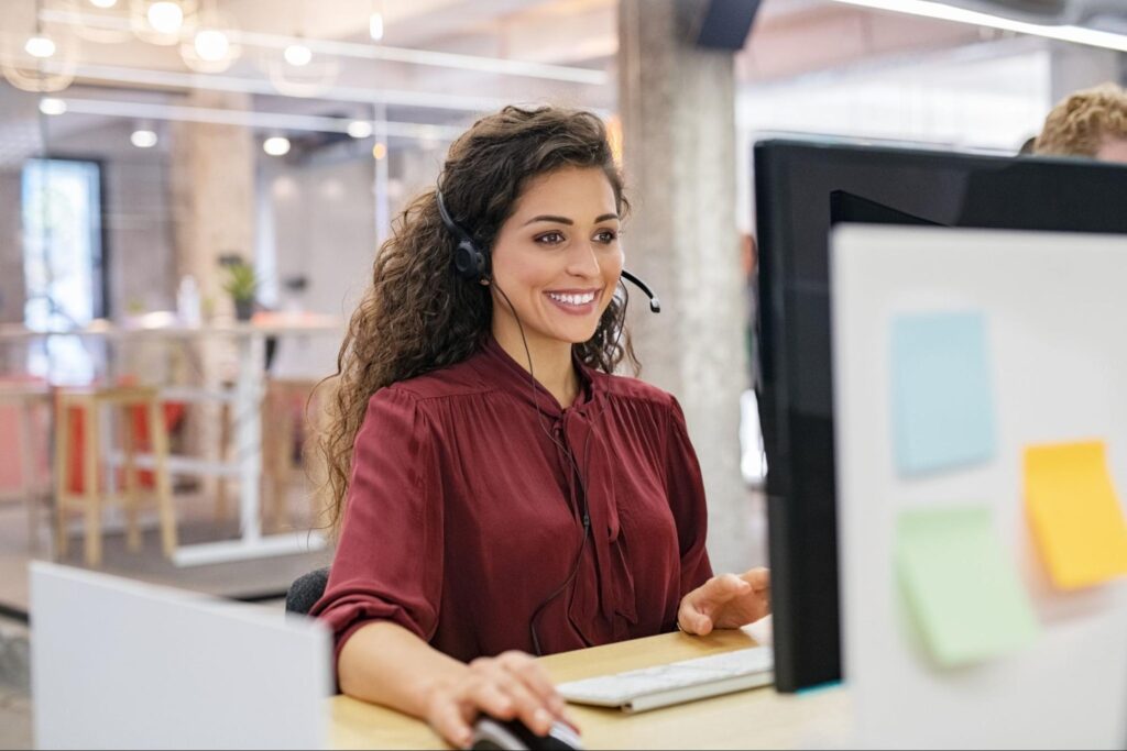 smiling female customer service agent wearing headset working at computer